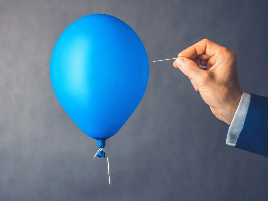 Picture of someone about to pop a balloon with a pin.