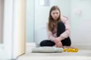 Photo of a girl with an eating disorder staring at a bathroom scale.