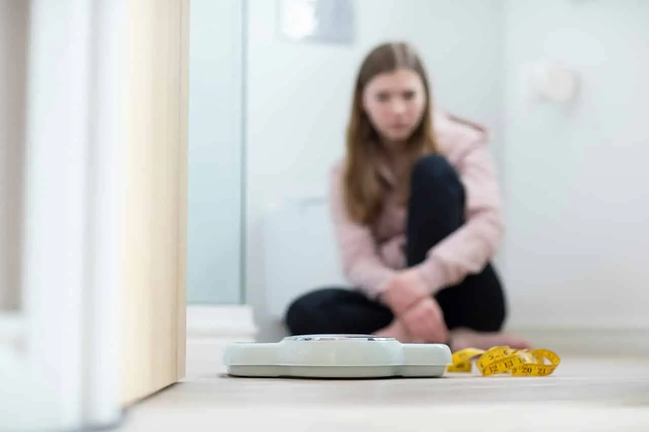 Photo of a girl with an eating disorder staring at a bathroom scale.