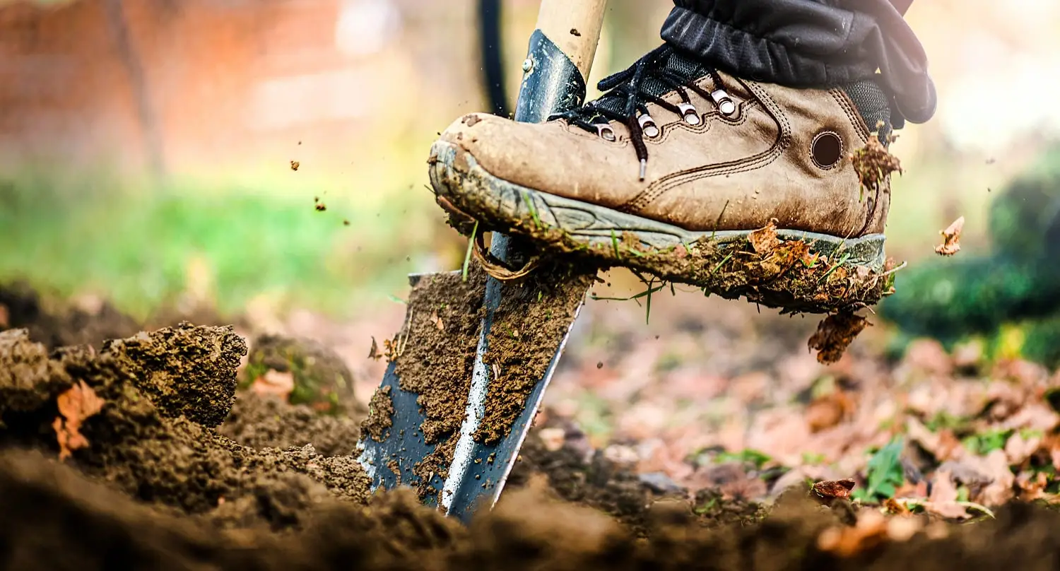 Photo of a man digging a hole by using a shovel.