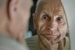 Photo of an older man looking at a mirror.