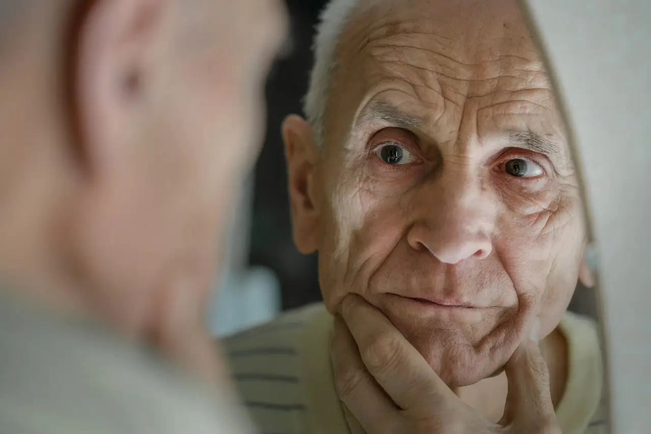 Photo of an older man looking at a mirror.