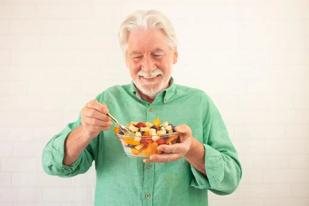Photo of an older man eating a bowl of fruit.