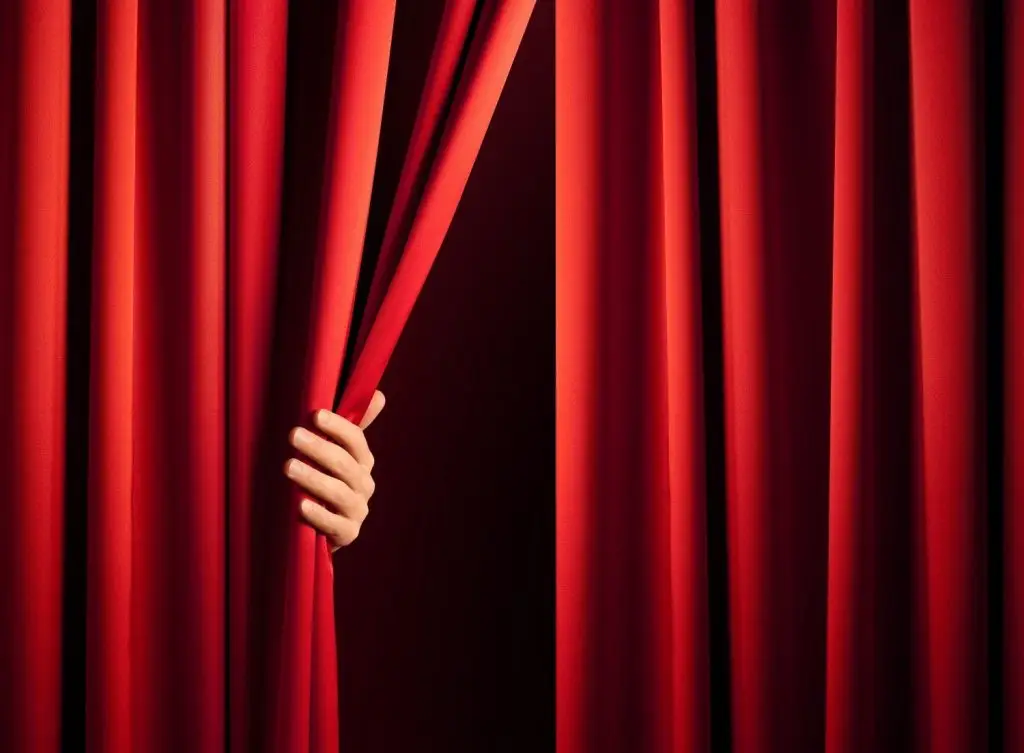 Photo of someone pulling a theater curtain open to start the second act.