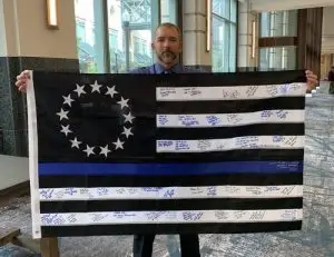 Photo of Chris Hoyer holding a Thing Blue Line flag signed by police officers, veterans and other members of the protective services.
