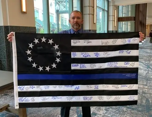 Photo of Chris Hoyer holding a Thing Blue Line flag signed by police officers, veterans and other members of the protective services.