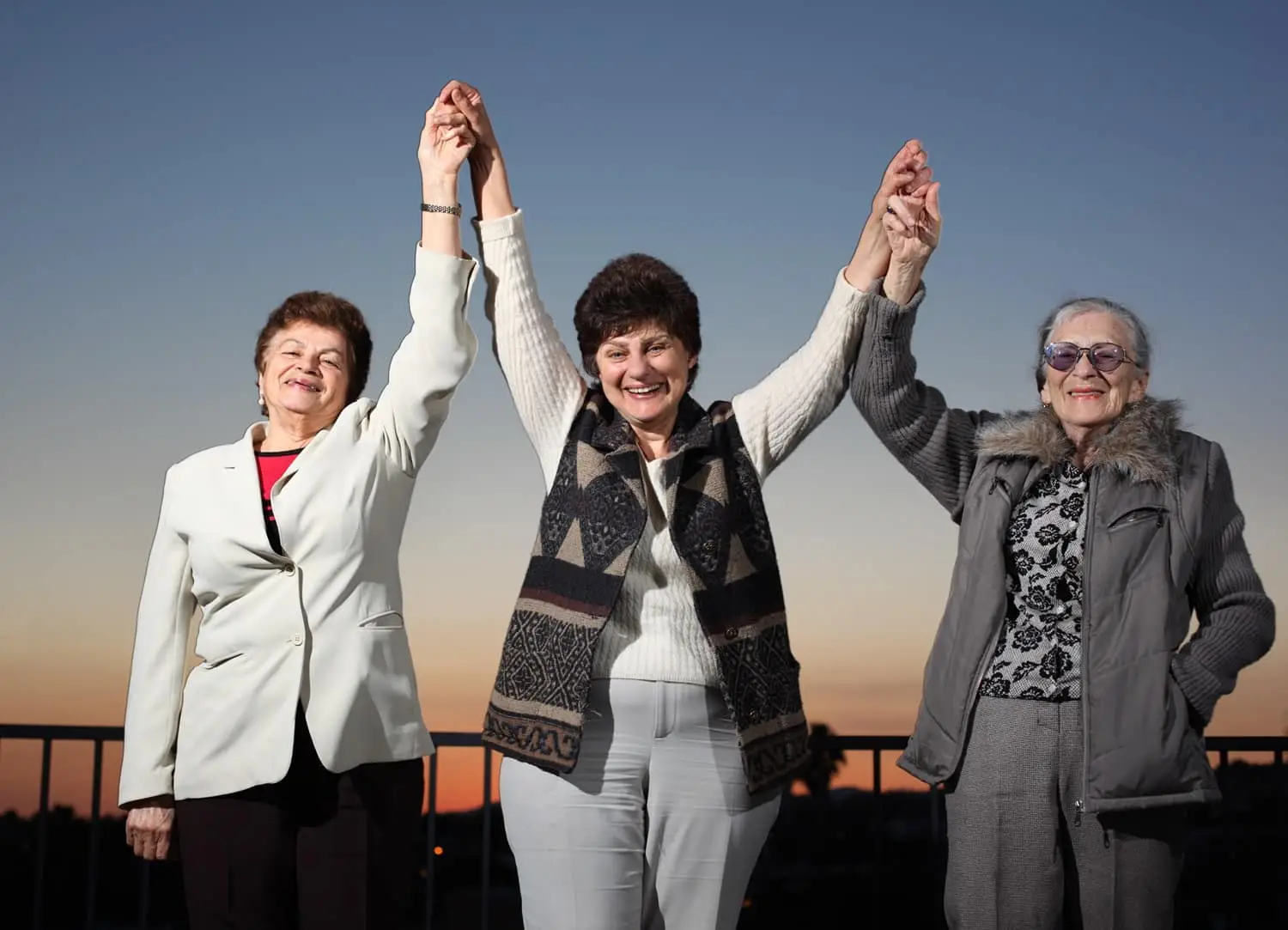 Photo of three older women united and raising hands in celebration.