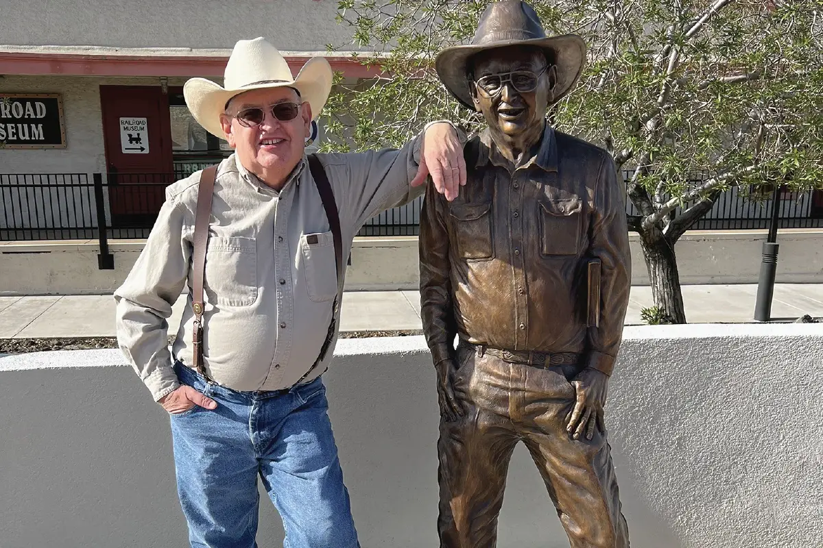 Jim Hinckley next to a statue of him in Kingman, Ariz.